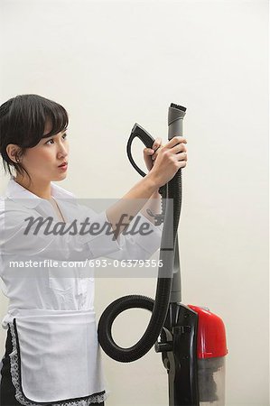Female housekeeper holding vacuum cleaner pipe against gray background