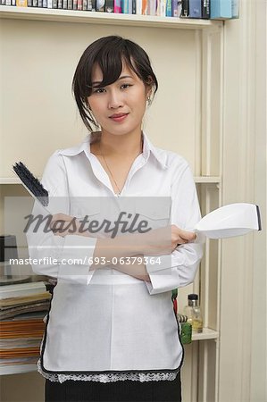 Portrait of young female housekeeper holding brush and dustpan