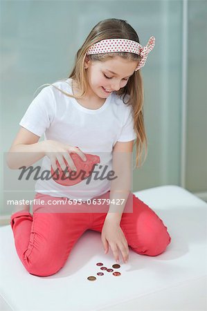 Young girl with piggy bank counting coins on bed