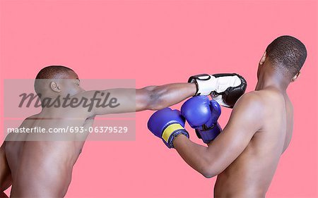 African American boxer punching opponent over pink background