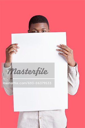 Portrait of a young man holding blank cardboard in front of face over pink background