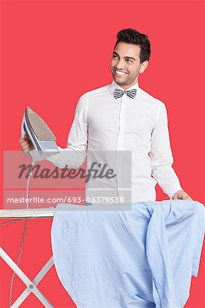 Happy man in formals ironing shirt over red background