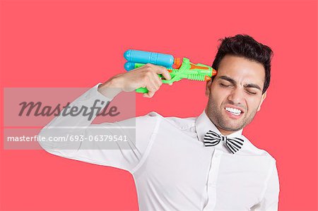 Frustrated man holding toy gun to his head over red background