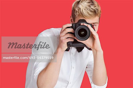 Young man taking picture with digital camera over red background