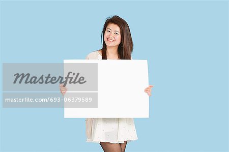 Portrait of a beautiful young woman holding blank cardboard over blue background