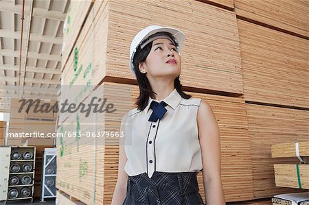 Young female industrial worker looking away with stacked wooden planks in background