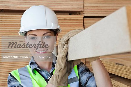 Portrait of female worker carrying wooden plank on shoulder