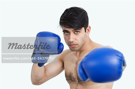 Portrait of an Indian shirtless man wearing blue boxing gloves against gray background