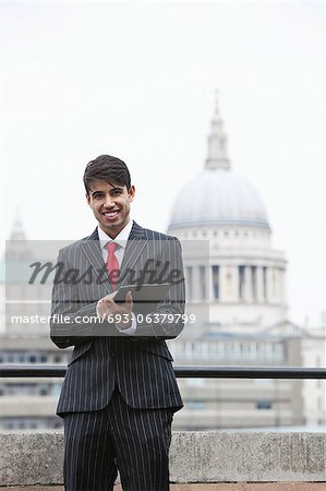 Portrait of a happy Indian businessman using tablet PC against St. Paul's Cathedral