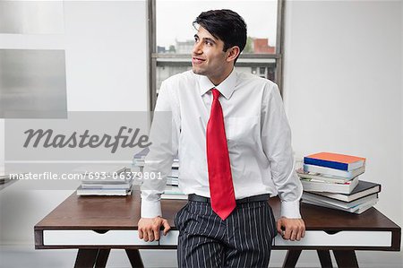 Indian businessman leaning on desk while looking away in office