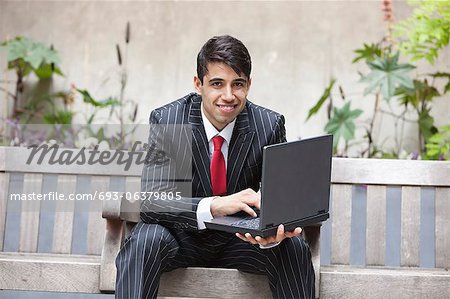 Young Indian businessman using laptop while sitting on bench