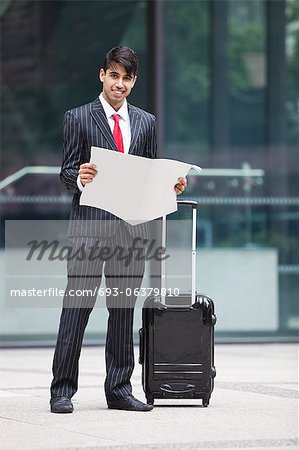 Young Indian businessman with luggage bag reading paper