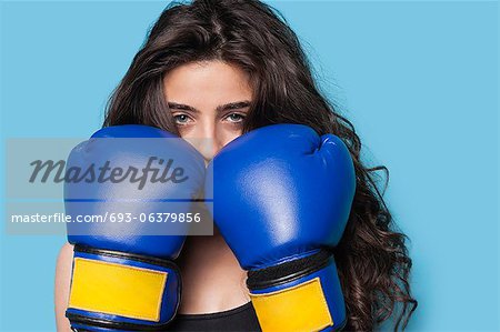 Portrait of a young female boxer with fists up against blue background
