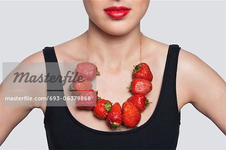 Mid section of a woman wearing strawberry necklace over gray background