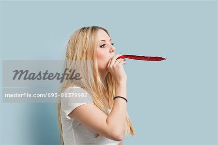 Young woman blowing party blower against light blue background