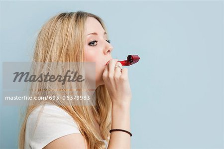Young woman with party blower against light blue background