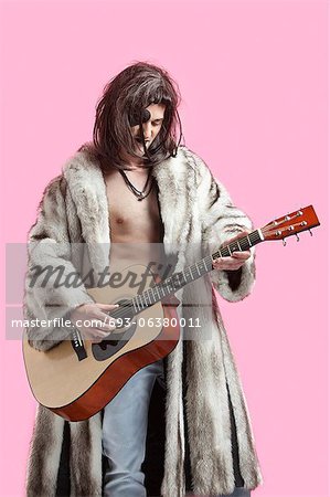 Young man in fur coat playing guitar against pink background