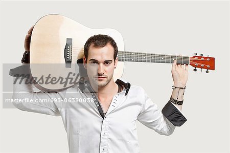 Portrait of young man carrying guitar over his shoulder against gray background