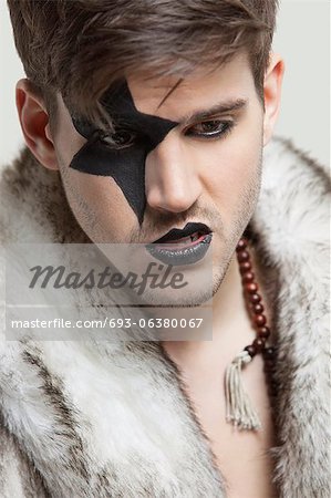 Angry young man with painted face wearing fur coat against gray background