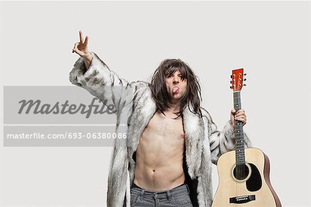 Young man in fur coat holding guitar while gesturing over gray background