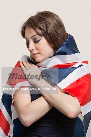 Young woman wrapped in British Flag over gray background
