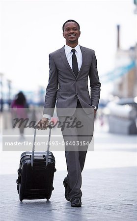 Portrait of African American businessman smiling and pulling suitcase