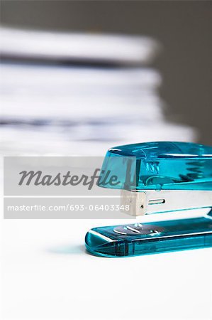 Blue stapler on table with stack of papers in background