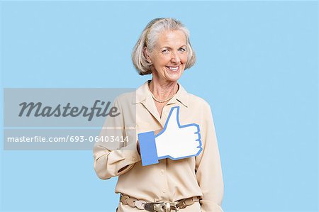 Portrait of senior woman in casuals holding fake like button against blue background