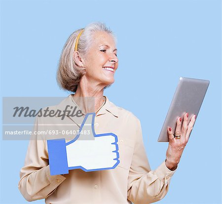 Senior woman with tablet PC holding fake like button against blue background