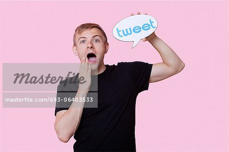 Portrait of surprised young man holding tweet bubble against pink background