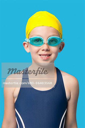 portrait of a happy young girl wearing swim goggles over blue background