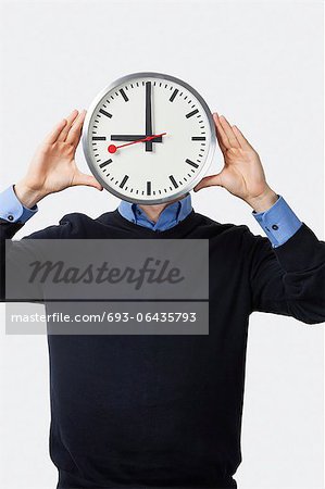 Young man covering his face with clock standing against white background