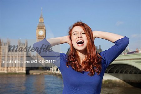 Angry young woman with hands on head screaming against Big Ben clock tower, London, UK