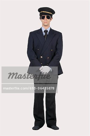 Full length of young man in pilot uniform standing against gray background