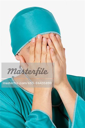 An upset male surgeon covering face with hands against gray background