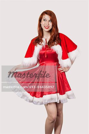 Happy young woman in Santa costume standing against gray background