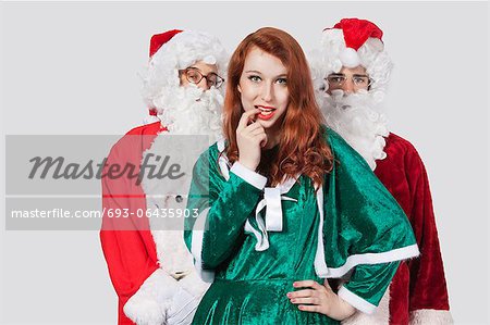 Portrait of young men in Santa costume standing with woman against gray background