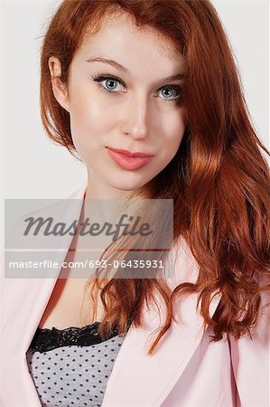 Portrait of beautiful young businesswoman in pink suit against gray background