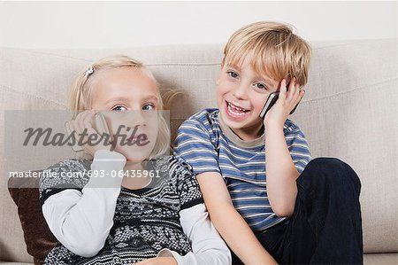 Happy brother and sister using cell phones at home