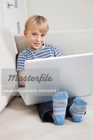 Portrait of happy young boy using laptop on sofa