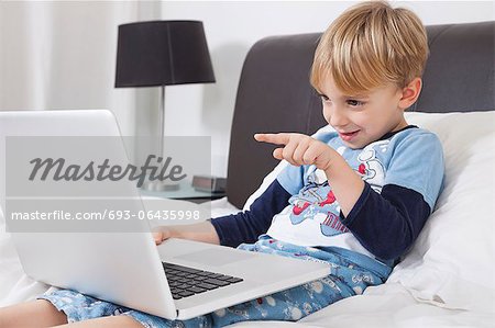 Playful Caucasian boy using laptop computer in bed