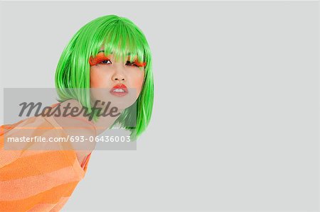 Portrait of young woman wearing green wig over gray background