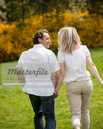 Couple holding hands with back to camera running through park