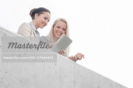 Low angle view of young businesswomen using digital tablet on office terrace against sky
