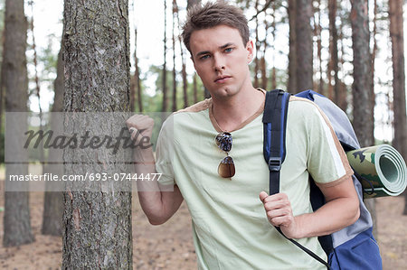Portrait of handsome young man with backpack hiking in forest