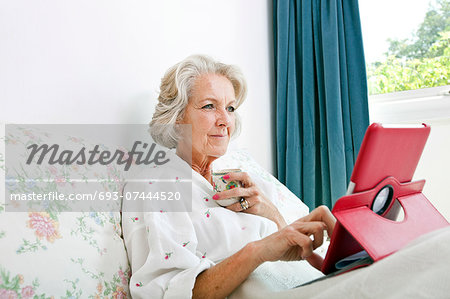 Senior woman using digital tablet while having coffee on bed at home