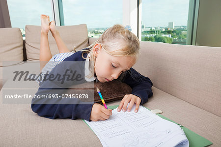 Little girl doing mathematics homework on sofa