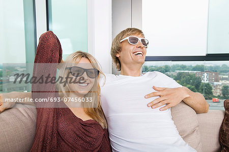Happy couple wearing 3D glasses while sitting on sofa at home