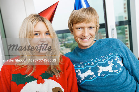 Portrait of smiling couple wearing Christmas sweaters and party hats in living room at home