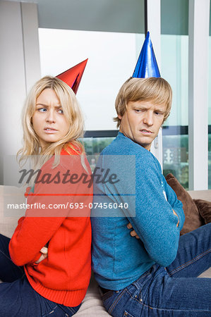 Side view of annoyed couple in Christmas sweaters and party hats sitting back to back at home